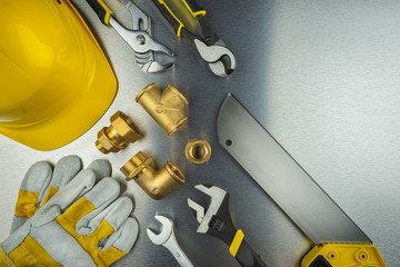 Plumber tools on brushed aluminum background with yellow helmet
