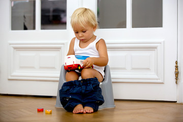 Infant child baby boy toddler sitting on potty, playing with toys in living room