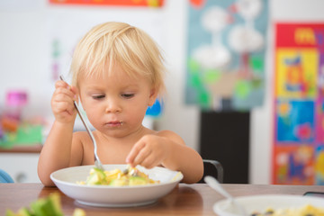 Sweet toddler boy, eating spaghetti at home, making a mess and having fun