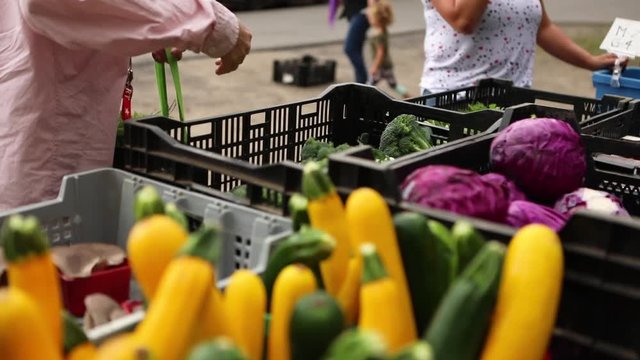 Close up and slow motion footage of a person shopping at a local farmers market, placing broccoli and red cabbage into a reusable shopping bag 