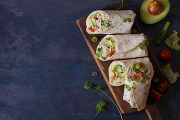 Chicken wraps with avocado, tomatoes and iceberg lettuce. Tortilla, burritos, sandwiches, twisted rolls. View from above, top, copy text - obrazy, fototapety, plakaty