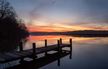 Fototapeta na wymiar Dock on a River Shore with Colorful Dawn Sky and Calm Water with Reflections