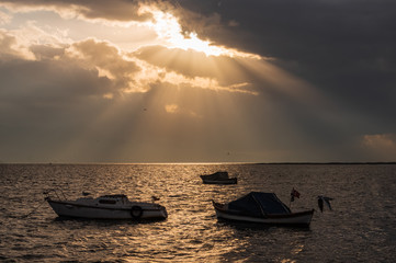 Silhouettes of seagull and light seeping through the clouds at sunset. Silhouettes of boats in reverse light. Dramatic themed studies are appropriate.