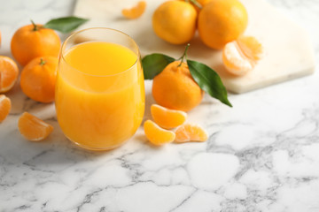 Glass of fresh tangerine juice and fruits on marble table. Space for text