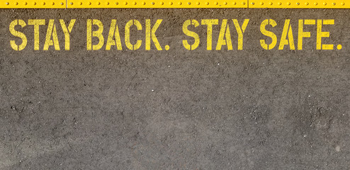 yellow sign at train station asking people to stay back, stay safe, on concrete floor