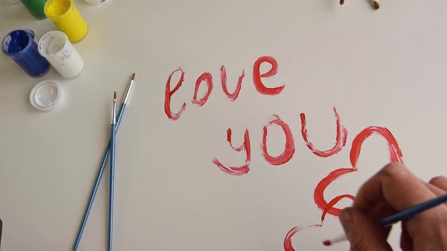 Top view of woman hand painting "I love you" text on white background, artistic creative occupation, love concept