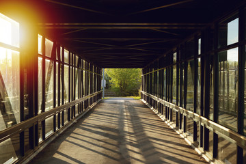 Obraz premium pedestrian pathway above highway, golden light shining creating shadows. green forest in the end, strong light on border