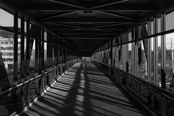 Fototapeta premium pedestrian pathway above highway, golden light shining creating shadows. Black and white.