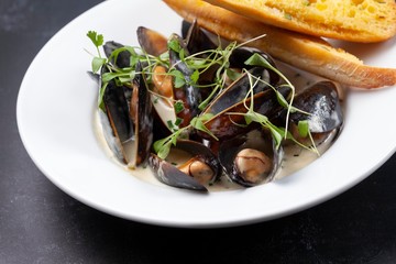 Mussels in a white wine sauce with garlic bread in a white dish