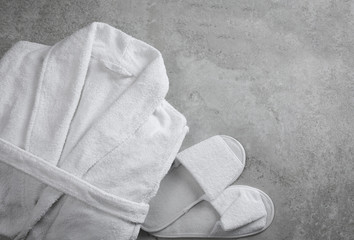 Clean folded bathrobe and slippers on grey stone background, flat lay
