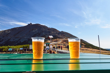 Plastic beer mugs with beer on the table against the background of the Sniezka mountain peak in...