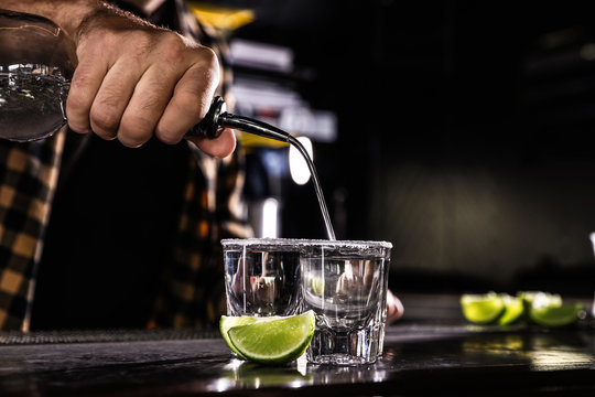 Bartender pouring Mexican Tequila into shot glasses at bar counter, closeup