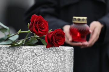 Woman with candle outdoors, focus on red roses. Funeral ceremony