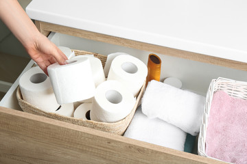 Woman taking toilet paper roll from cabinet drawer, closeup
