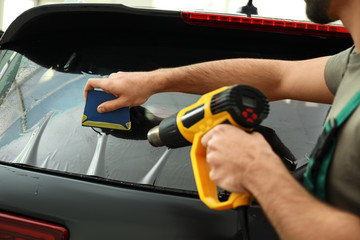 Worker tinting car window with heat gun in workshop, closeup