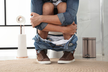 Man suffering from hemorrhoid on toilet bowl in rest room, closeup