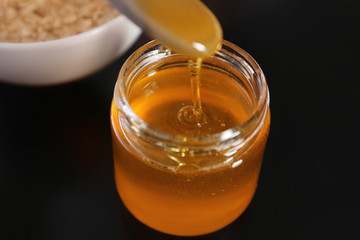 Spoon with honey over jar on black table, closeup