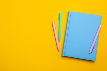 Light blue notebook and pens on yellow background, flat lay. Space for text