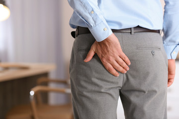 Man suffering from hemorrhoid in office, closeup