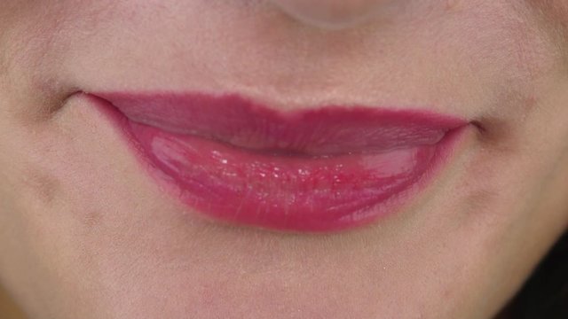 Woman with amazing white straight teeth due to dental veneers bites lips and smiles extreme slow motion close view