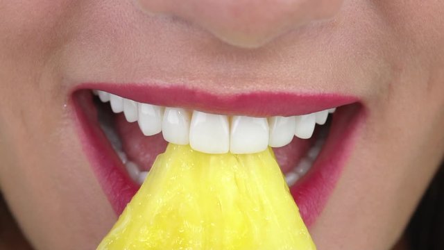 Beautiful woman with white dental veneers smiles amazingly and bites big juicy pineapple slice slow motion closeup