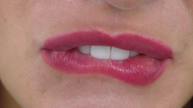 Woman with amazing white straight teeth due to dental veneers bites lips and smiles extreme slow motion close view