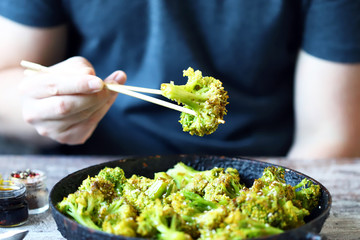 Broccoli cooked in a pan. Healthly food. A man with chopsticks eats broccoli.