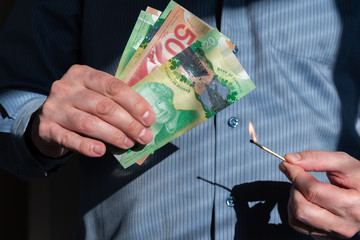 Close-up of man's hands holding burning match near Canadian dollars