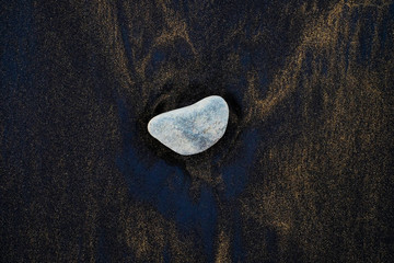 One big stone isolated on a backdrop of dark volcanic sand.