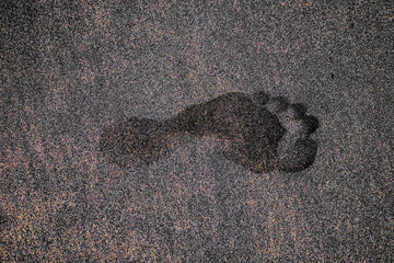 Single deep left human foot print in dark volcanic sand.