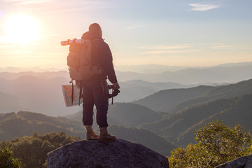 Young man with backpack enjoying sunset on binoculars peak of mountain layers line.Travel hiking.