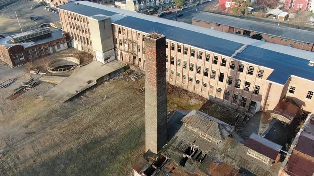 Aerial orbiting shot around brick chimney at old closed factory building, site of former silk mill