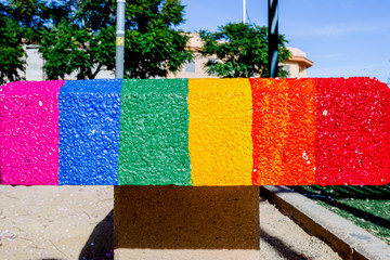 Gay flag painted on the hard cement of a stone bench.