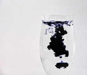 Blue and black ink dropping into a wine glass of water on a white background.