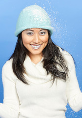 Stunning young Asian woman in winter scene - shot in studio against blue background - wearing thick sweater, cap and with light blue lipstick and eye shadow fake snow falling