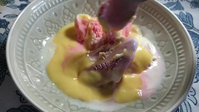 Strawberry, vanilla and black current flavored ice cream with yellow vanilla custard topping, delicious sunday dessert being scooped with stainless steel spoon in porcelain bowl.