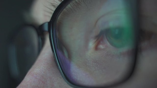 Close up macro view of young man in glasses eye moving fast staring at addictive video games and the bright screen of a computer