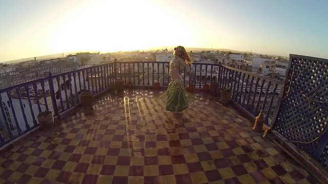 Camera pushes in on slow motion of belly dancer backlit by the setting sun in Essaouira, Morocco.