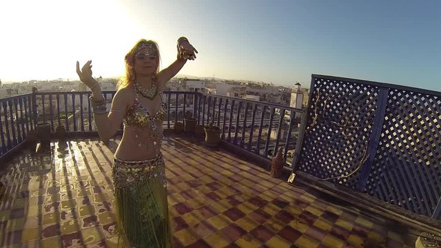 Closeup of beautiful blonde belly dancer on the roof of a building at sunset doing snake arms.