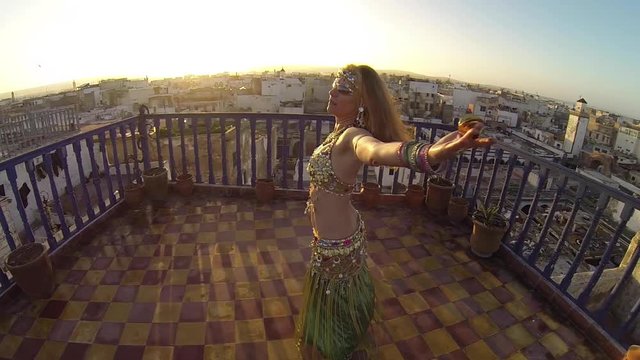 High angle looking down on belly dancer as she spins on the roof of a building in Morocco at sunset.