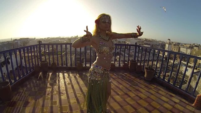 Beautiful blond belly dance on the roof of a building in Morocco dancing at sunset.