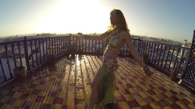 Closeup of backlit belly dancer dancing on the roof of a building in Morocco at sunset.