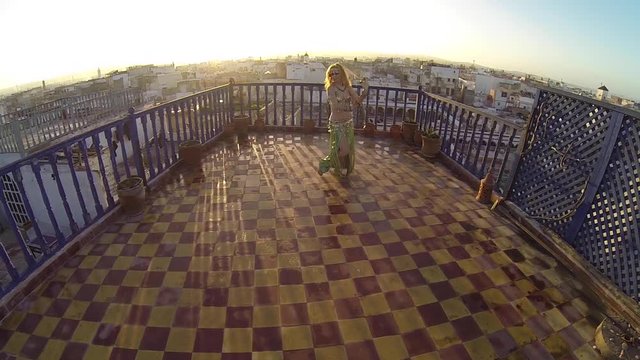 Camera pushes in on slow motion of belly dancer backlit by the setting sun in Essaouira, Morocco.