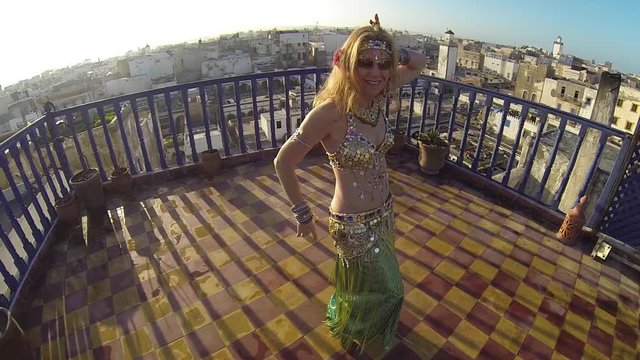 Belly dancer at sunset in Morocco on the roof of a building doing undulations.
