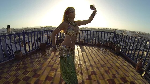 Slow motion of dancer doing Egyptian movements as she performs during sunset on a rooftop in Essaouira, Morocco.
