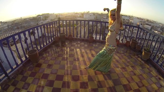 Smiling and happy belly dancer on the roof of a building in Morocco at sunset doing an Egyptian move.