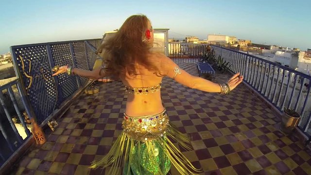 Camer circles beautiful belly dancer as she spin at sunset on the roof of a building in Morocco.