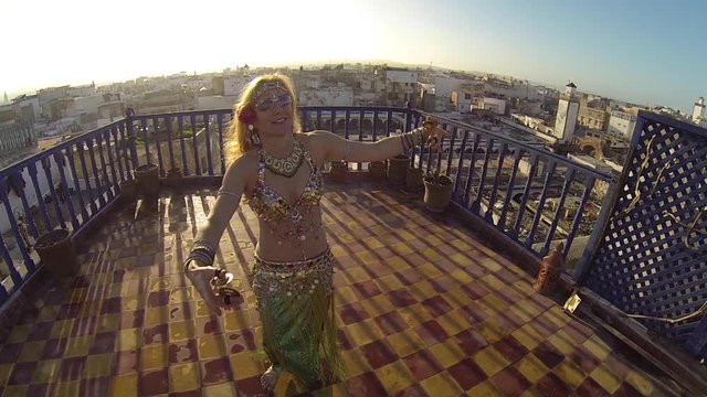 Belly dancer smiles at sunset as she dances on a rooftop in Morocco.