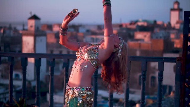 Beautiful belly dancer doing back bend at sunset performing on a rooftop in Morocco.