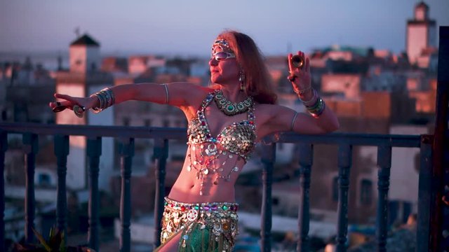 Beautiful belly dancer doing snake arms at sunset performing on a rooftop in Morocco.